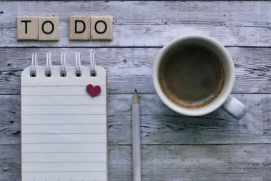 To do list, coffee, and pencil on wooden background.